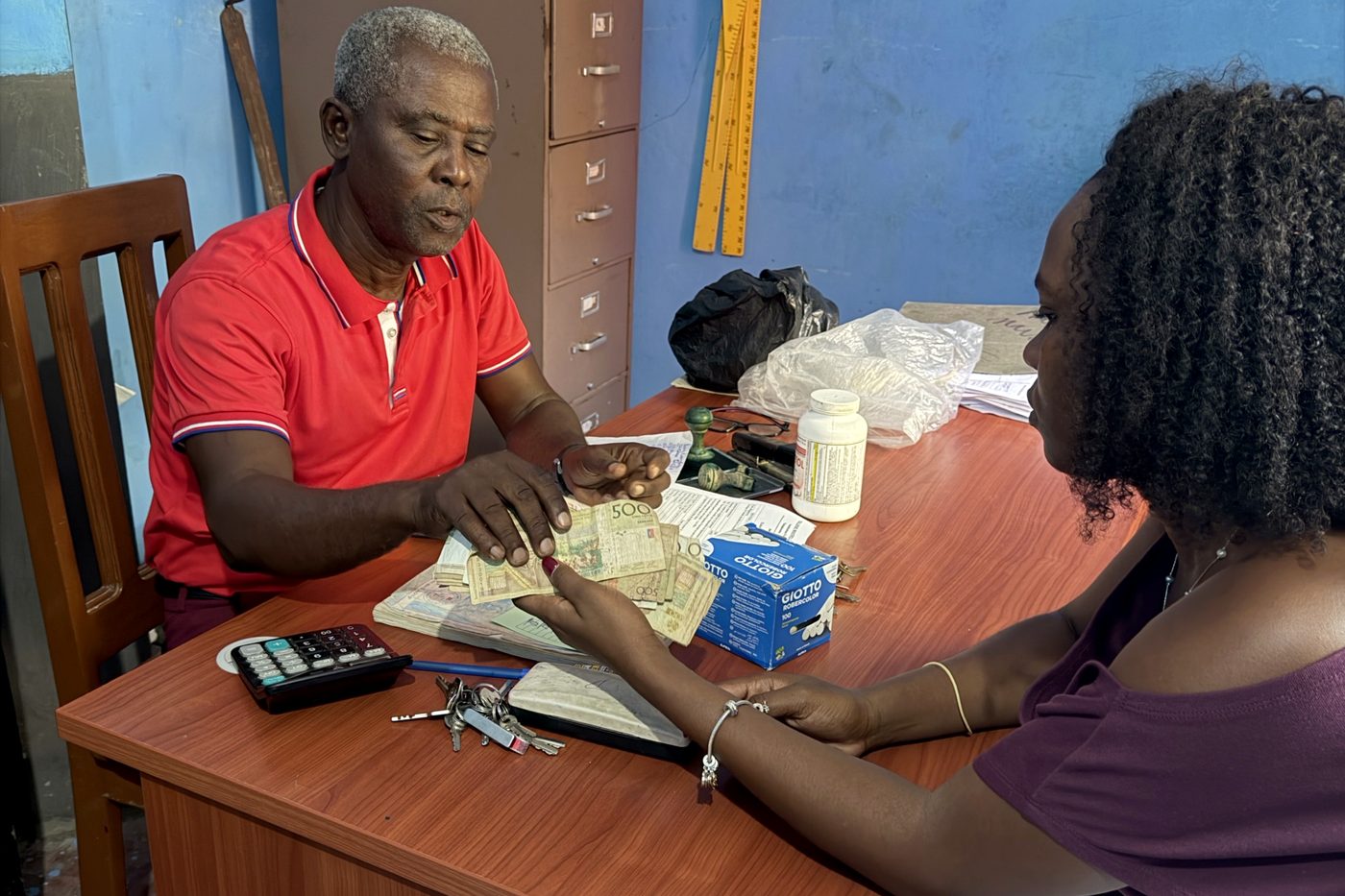 A school director counts a tuition payment at his desk while an HCTF coordinator waits for the receipt.
