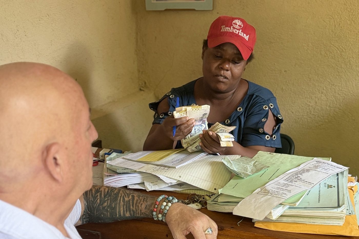 A second school office in Cap-Haïtien, where staff count the tuition payment beside a stack of student files.