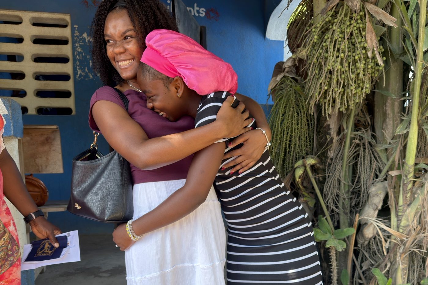 An HCTF coordinator is embraced by a student outside a school in Cap-Haïtien after her fees are confirmed.